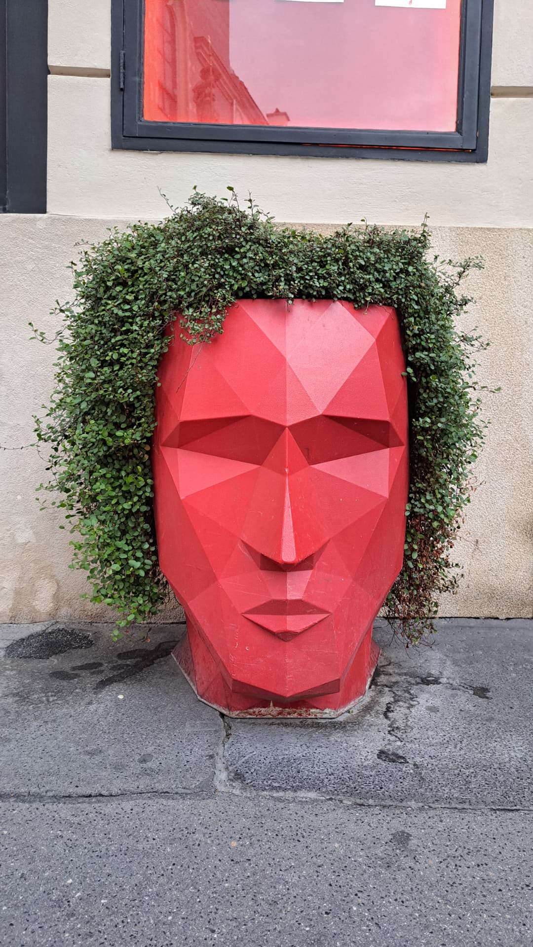 A red sculpted face planter with green plants for hair