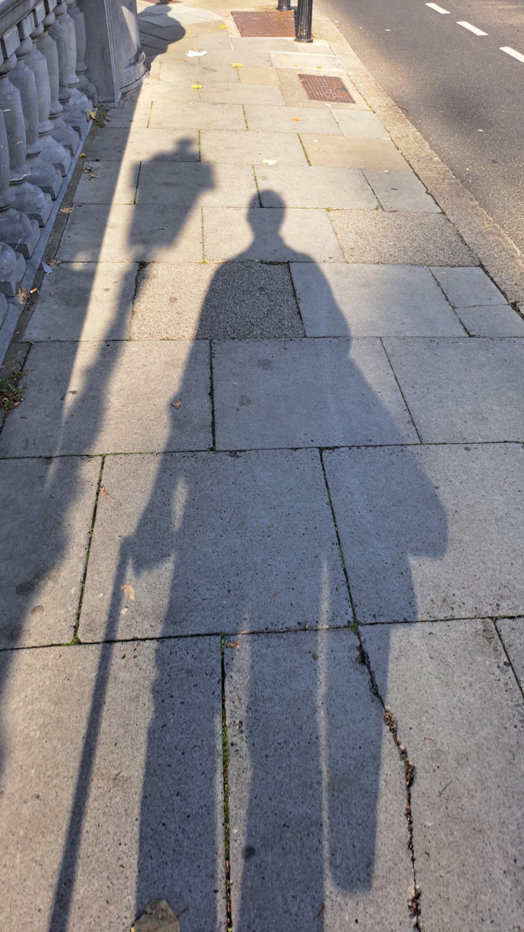 A long shadow of a photographer on a sunlit pavement